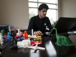 Rajeev Kulkarni, vice president and general manager consumer solutions at 3D Systems Corporation, works at his desk while surrounded by objects created on a 3-D home printer.